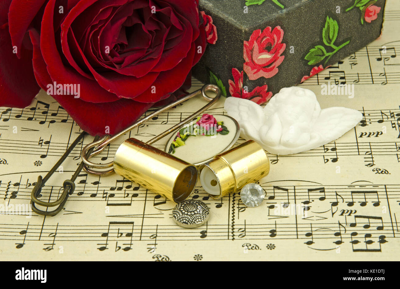 Stillleben mit roter Rose und Engel unter mehreren Haarnadeln, Geschenk, Felder und Schaltflächen auf dem Hintergrund der Zettel mit Notizen Stockfoto