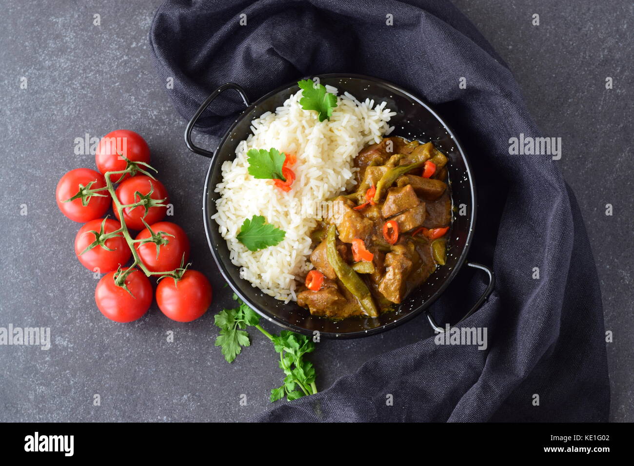 Schweinefleisch in pikanter Sauce curry mit Auberginen und grüne Bohnen, mit gekochten Reis in einer Black Metal Schüssel auf einem grauen Abstrakt Hintergrund serviert. Hausmannskost. Stockfoto