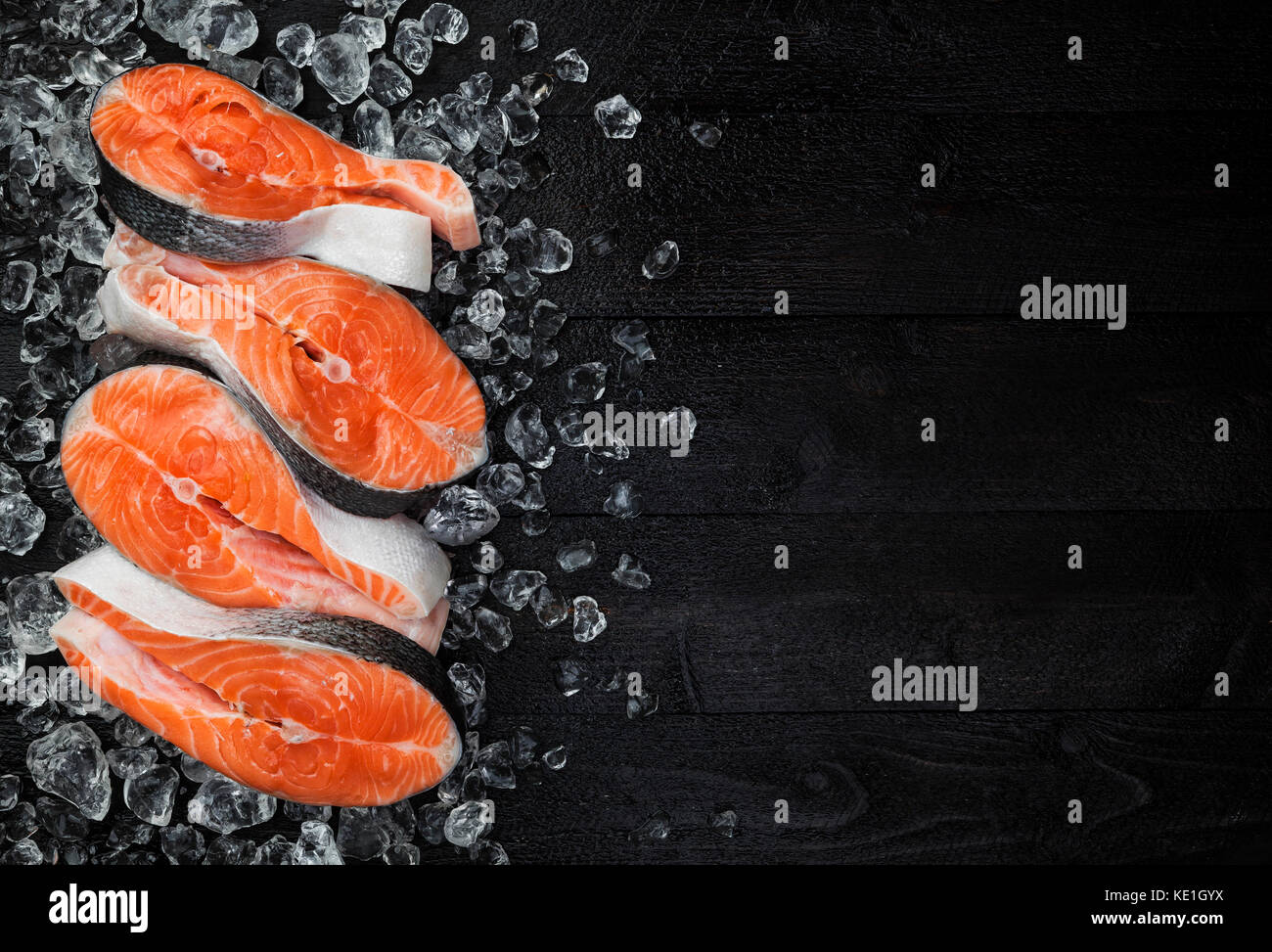 Lachssteak auf Eis auf schwarzen Holztisch Draufsicht, Fisch essen Konzept. Kopieren Sie Platz Stockfoto
