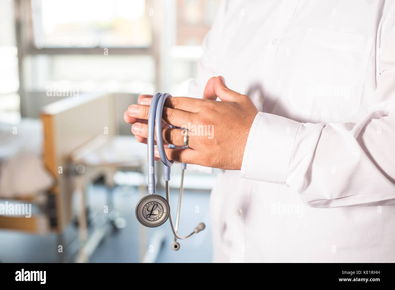 Ärzte Hände halten ein stethescope im Gebet Position mit Krankenstation in hinten Stockfoto