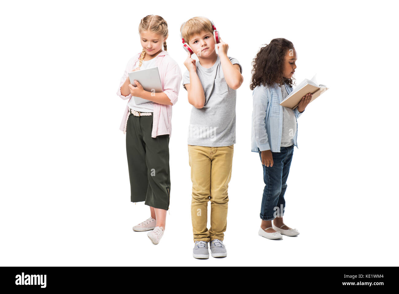 Adorable multiethnischen Kinder Musik hören über Kopfhörer, mit digitalen Tablet und lesen Buch isoliert auf weißem Stockfoto
