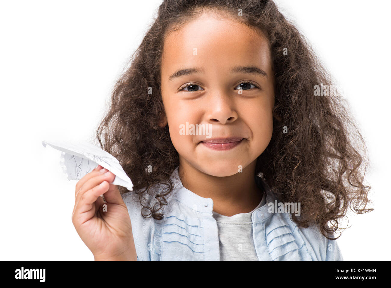 Cute African American Girl holding Paper Plane und lächelnd an der Kamera auf Weiß isoliert Stockfoto