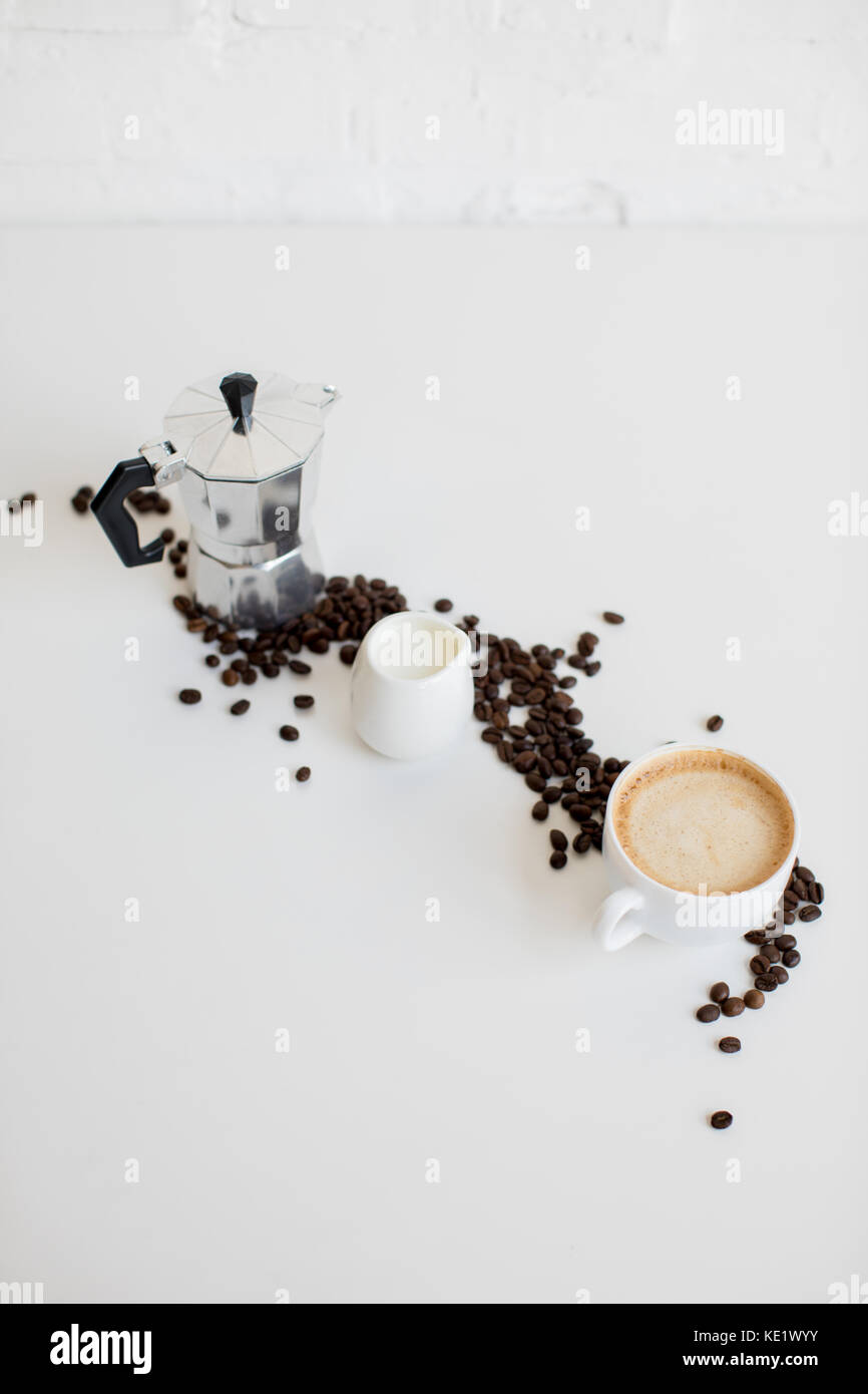 Französische Presse, Tasse Kaffee und Milch Glas mit verstreute Kaffeebohnen auf weißen Tischplatte Stockfoto