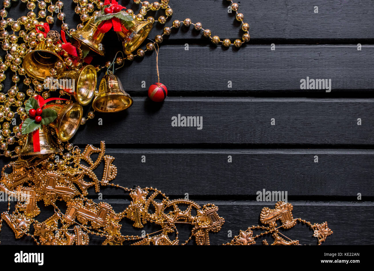 Weihnachtsdekoration Hintergrund, auf einem schwarzen Hintergrund Holz, mit Glocken, Mistel, goldene Ketten, Kugeln und Requisiten und Kette mit Rentier, und Dekor Stockfoto