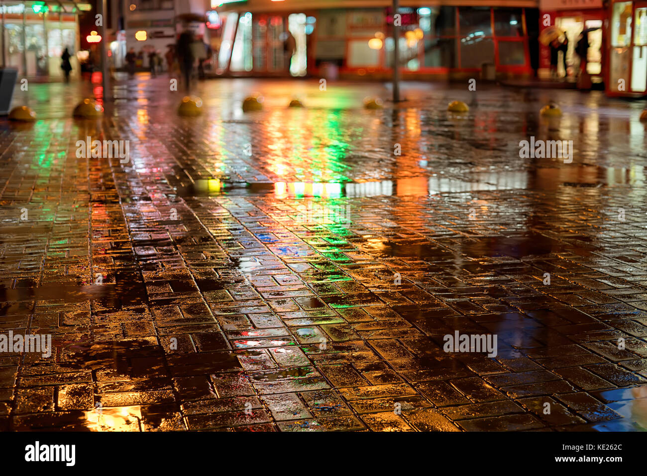 Regnerischen Nacht in der Stadt. nasse Straße, Farblicht Reflexion und verschwommene Silhouetten mit Sonnenschirmen. Stockfoto