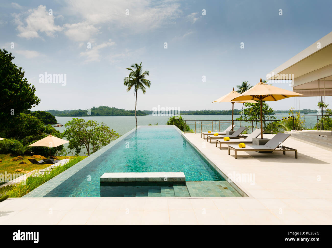 Infinity Pool mit Blick auf einen See, der von Palmen, Liegestühlen und Sonnenschirm grenzt, in der modernen Boutique Hotel Resort, Tangalle, Sri Lanka Stockfoto
