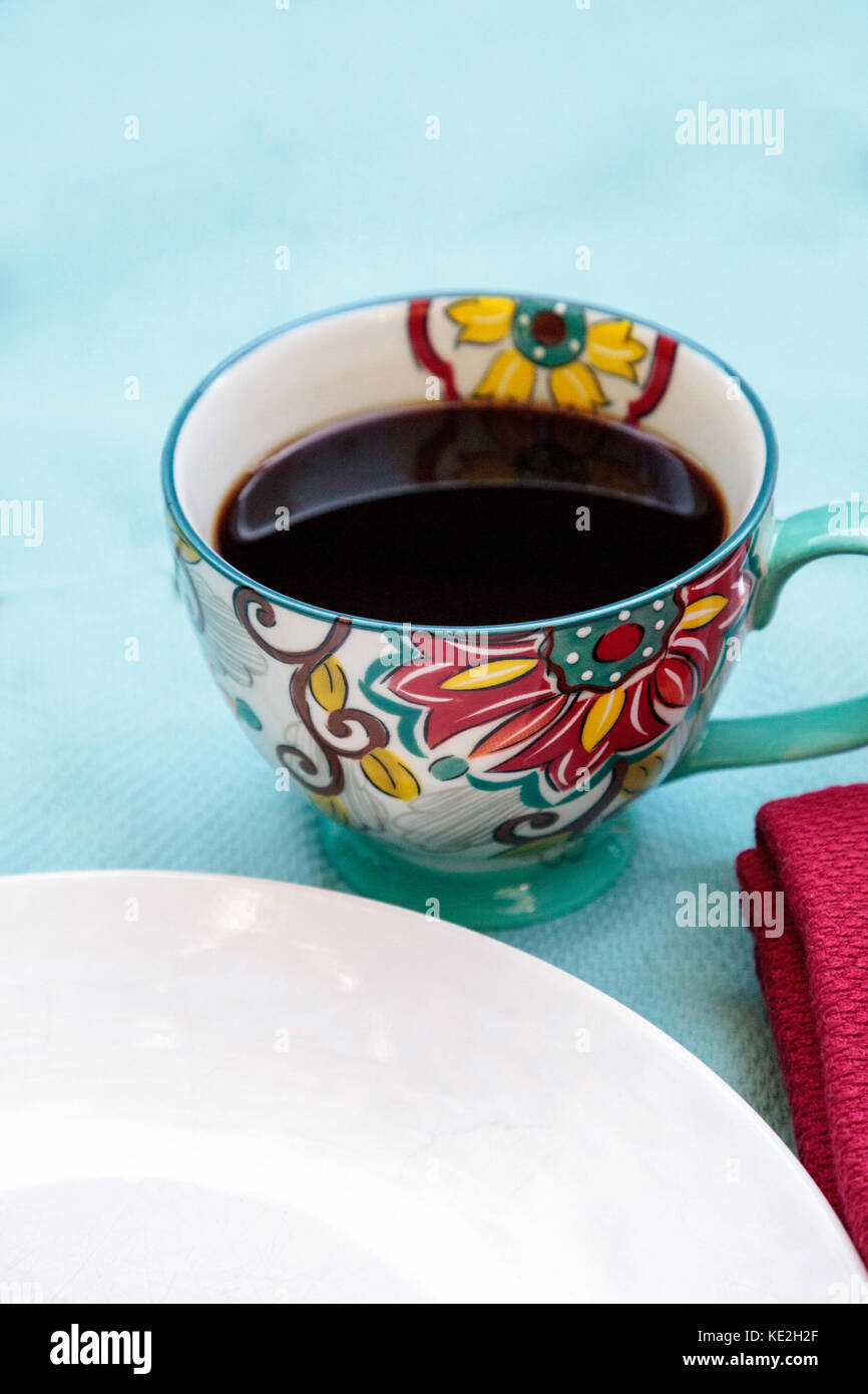 Schwarzen Kaffee in eine bunte Blume drucken Schale mit Orangensaft auf einem blauen Tischdecke Stockfoto