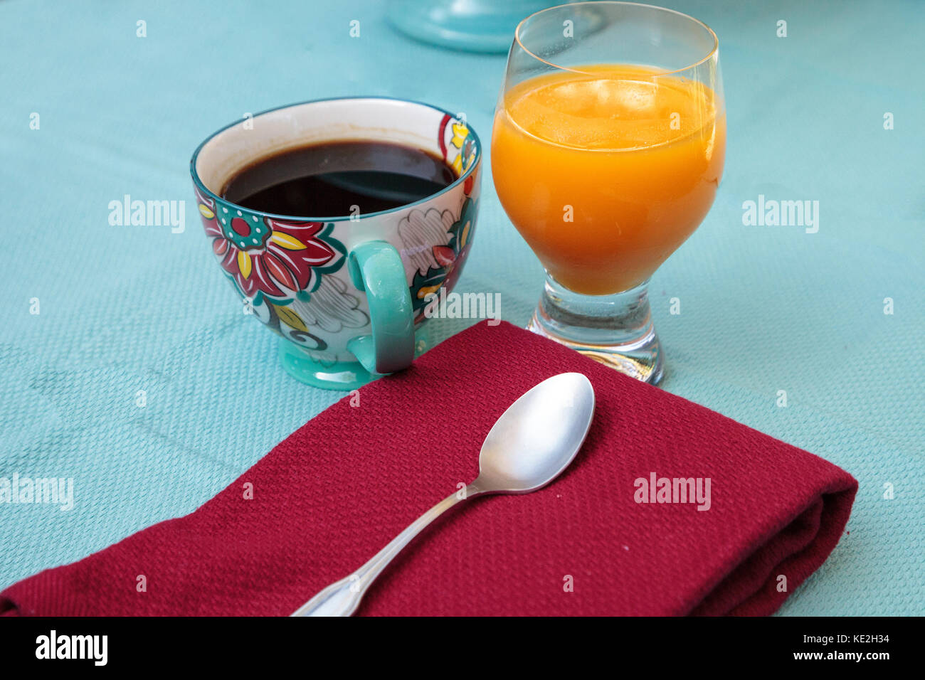 Schwarzen Kaffee in eine bunte Blume drucken Schale mit Orangensaft auf einem blauen Tischdecke Stockfoto