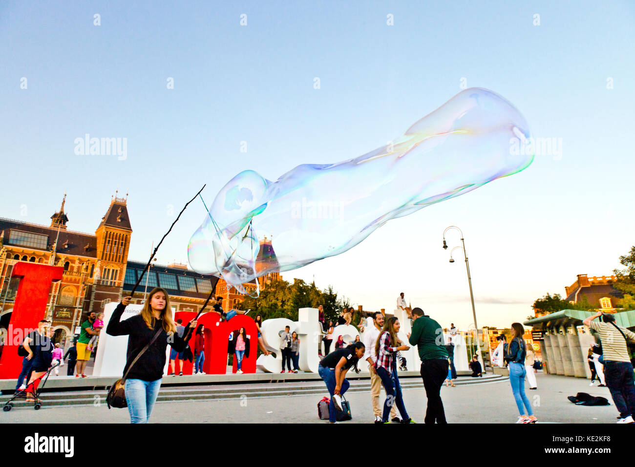 Eine Street Performer erzeugt eine gigantische Seifenblase in der Nähe der I Amsterdam Logo auf dem Museumplein in Amsterdam. Stockfoto
