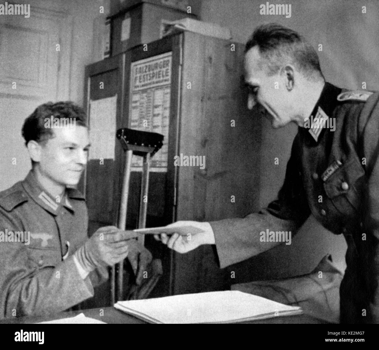 Salzburger Festspiele, 1941: Ein verwundeter Deutscher Soldat verkaufen, eine Eintrittskarte zu einem Konzert mit einem anderen Soldaten. Poster die Salzburg Festspiele" im Hintergrund. Stockfoto