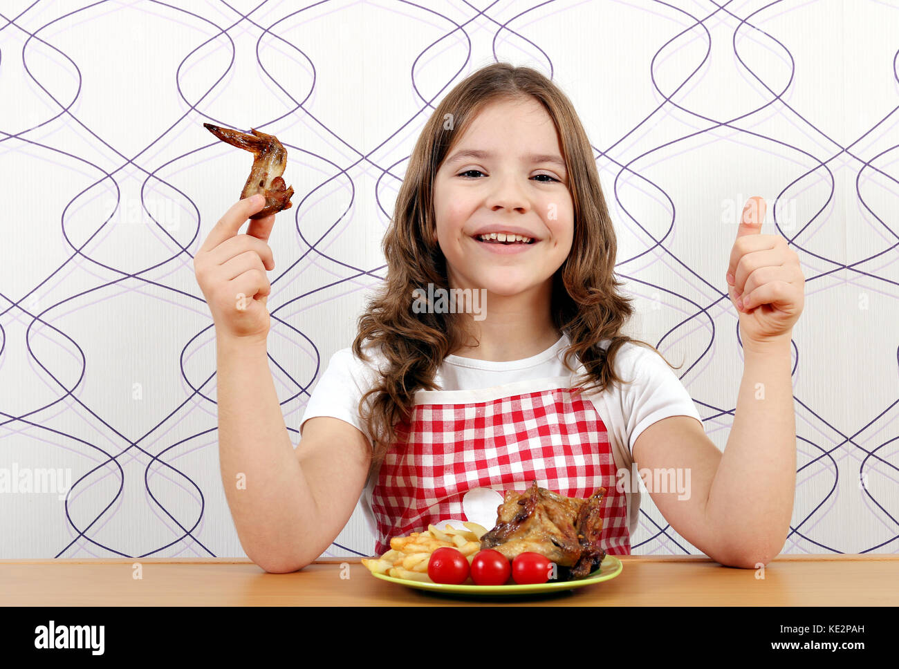 Glückliche kleine Mädchen mit gerösteten Chicken Wings und Daumen hoch Stockfoto