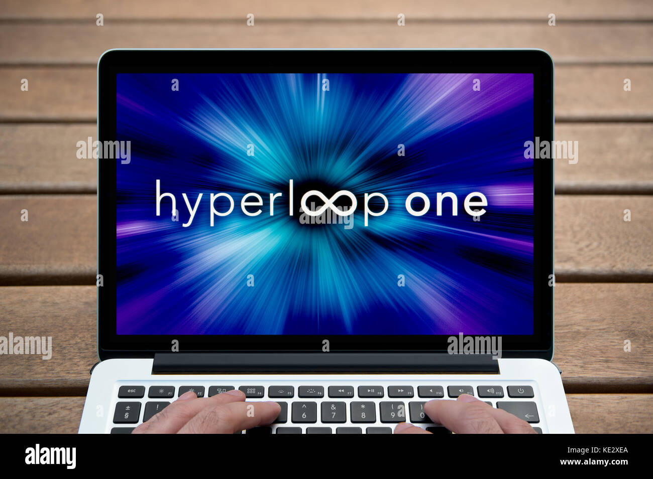 Die Hyperloop ein Logo wird auf dem Bildschirm des MacBook Pro Laptop gezeigt, Schuß gegen eine Holzbank einschließlich der Finger des Mannes (nur redaktionell). Stockfoto