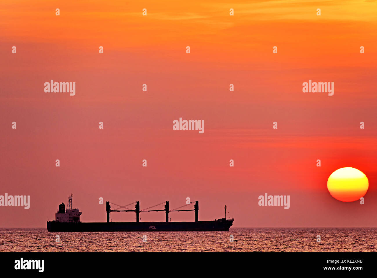 Roter Sonnenaufgang mit großer Sonne und PCL Kuok Frachtschiff in der Nordsee Stockfoto