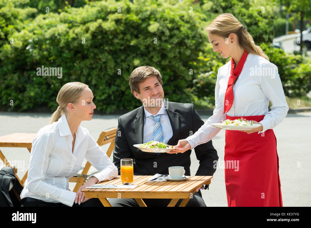 Junge Kellnerin das Essen zu den männlichen und weiblichen Unternehmer dienen Stockfoto