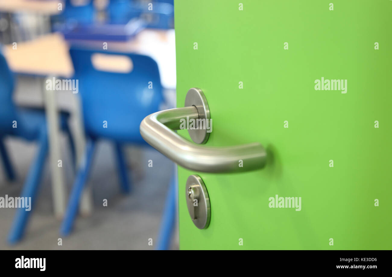 Nahaufnahme eines Türgriffs aus gebürstetem Stahl in einer britischen Schule. Die grüne Laminattür zeigt die Sitzplätze im Klassenzimmer Stockfoto