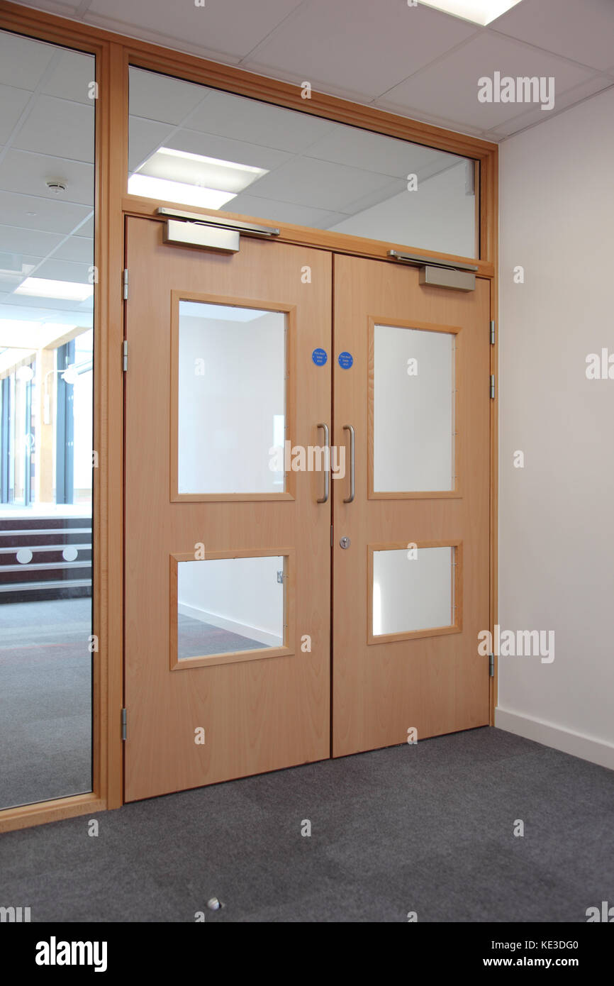 Geschlossene Brandschutztüren in einem Londoner Schulkorridor, Großbritannien. Zeigt verglaste Bildschirme über und an den seitlichen und kopfmontierten Verschließern. Stockfoto