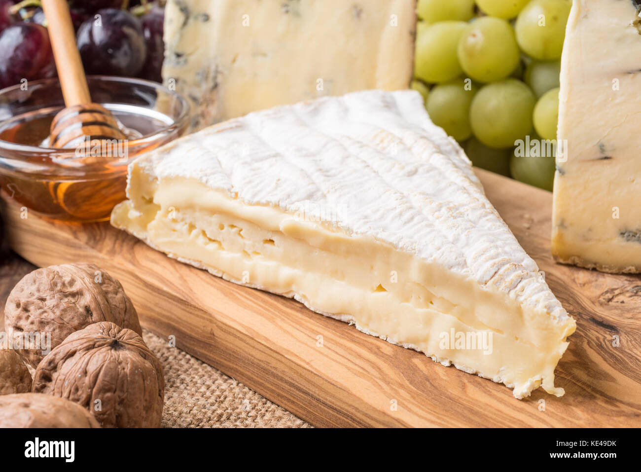 Holzbrett mit Käse, Weintrauben, Nüssen und Honig Stockfoto