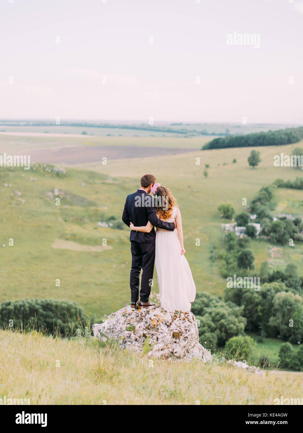 Romantische Rückansicht der hugging jungvermählte Paar stehend auf dem riesigen Stein und genießen die Natur. Stockfoto