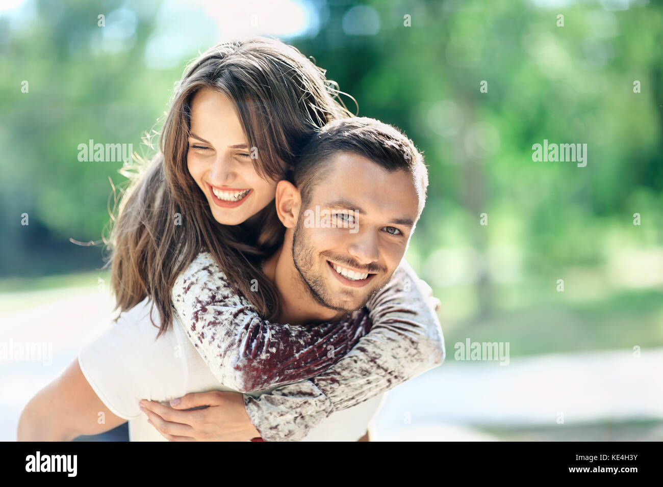 Im freien Portrait von Liebhaber glücklich, junger Mann und Frau an der Kamera schaut. Lächelnde Mädchen huckepack von ihrem Freund. Liebe, Jugend, Beziehung Konzept ph Stockfoto