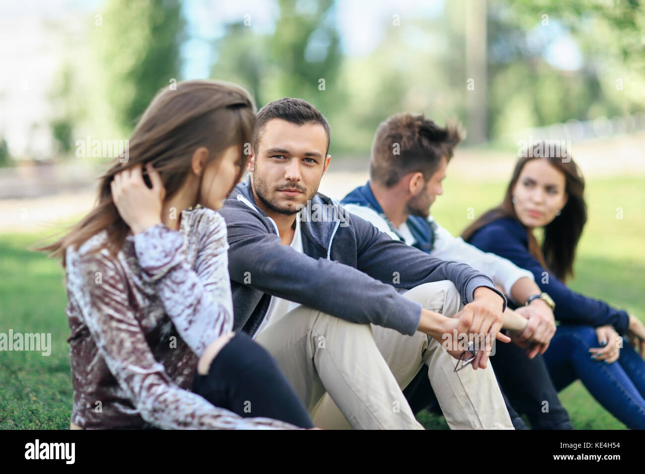 Junge Männer und Frauen reden und ruhen auf Rasen im Park an warmen, sonnigen Tag. Kaukasier, plaudernd im Freien. Beziehung, Freundschaft, Yout Stockfoto