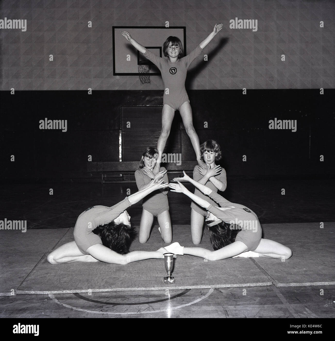 1960er Jahre, ein Bild aus der Mitte der 60er Jahre von fünf jungen weiblichen künstlerische Turnerinnen zeigen ihre Talente in der Schule Sporthalle und mit einer Trophäe, die Sie auf der Matte vor Ihnen, England, UK gewonnen haben. Stockfoto