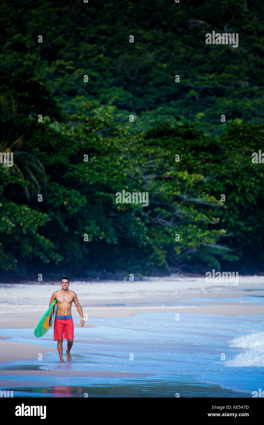 Auf unberührten Strand in Rio de Janeiro, Surfer, die seine Board, das zeigt eine brasilianische Flagge Stockfoto