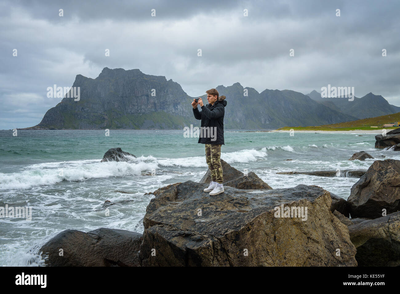 Junge nimmt Bilder auf einem Mobiltelefon an einem Strand im Norden von Norwegen Stockfoto