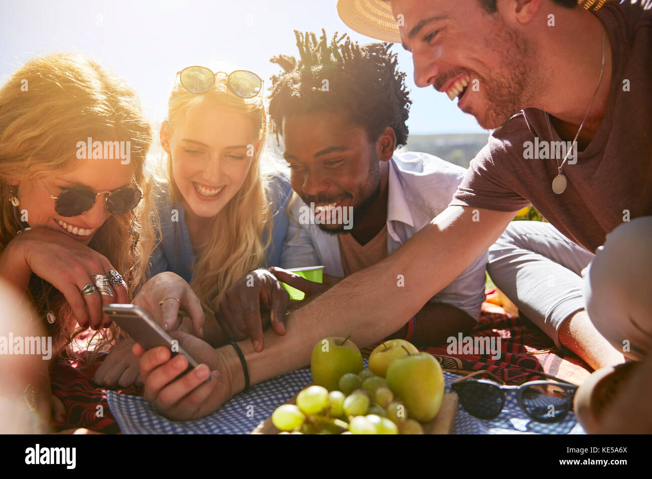 Junge Freunde schreiben mit Handy, genießen sonnigen Sommer Picknick Stockfoto