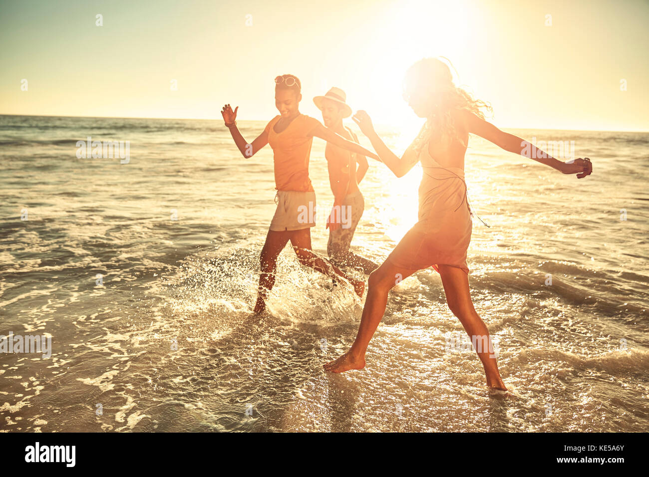 Verspielte junge Freunde planschen in sonnigen Sommer Meeresbrandung Stockfoto