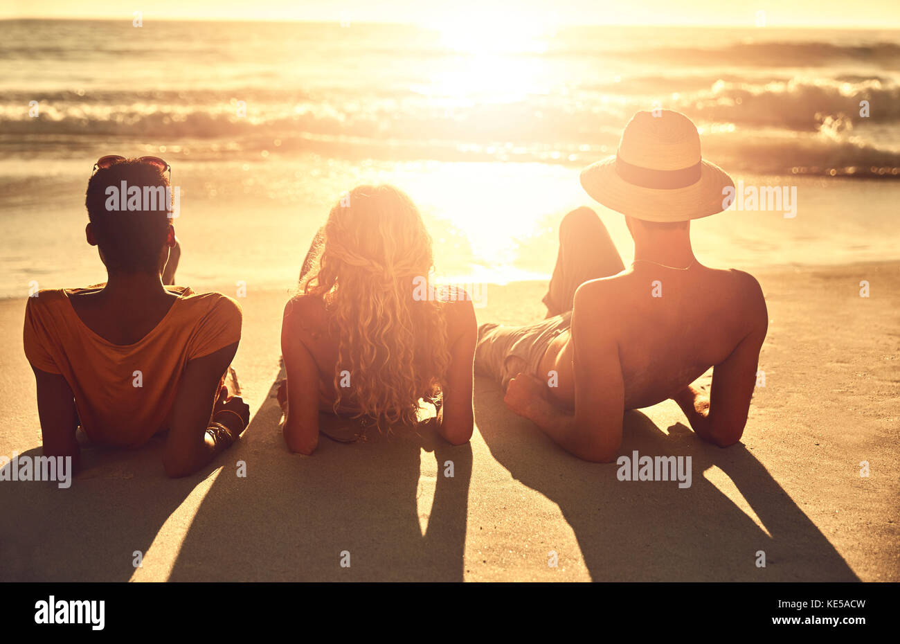 Unbeschwerte junge Freunde, die sich am sonnigen Sommersonnenuntergang am Meeresstrand entspannen Stockfoto