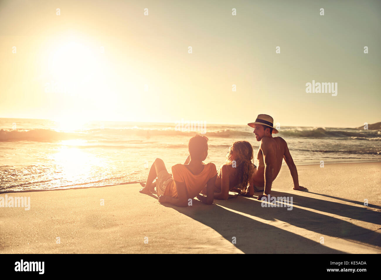 Junge Freunde entspannen am idyllischen, sonnigen Sommersonnenuntergang am Meeresstrand Stockfoto