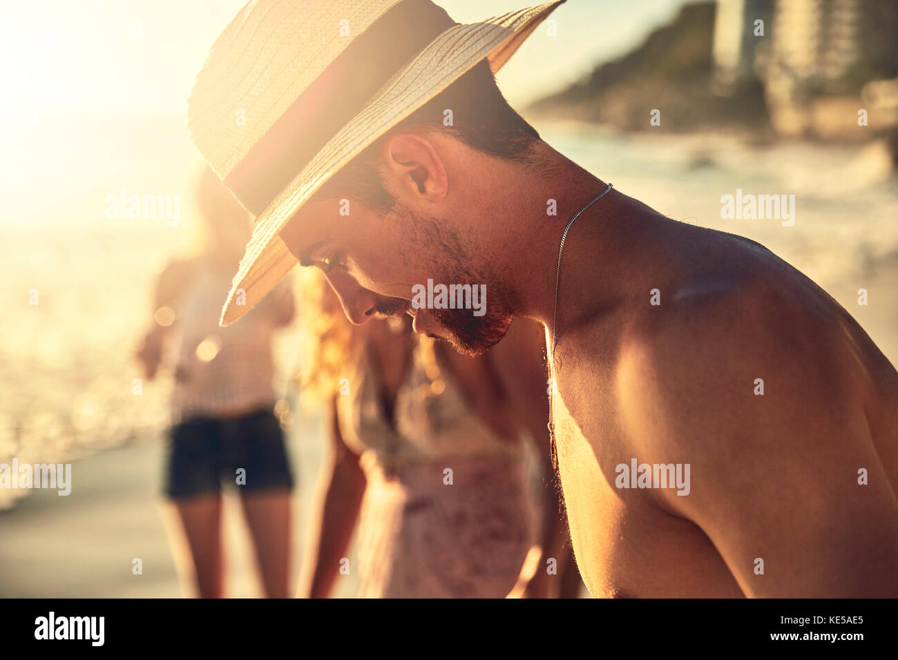 Junger Mann im Strohhut, der auf den sonnigen Sommer herabblickt Strand Stockfoto