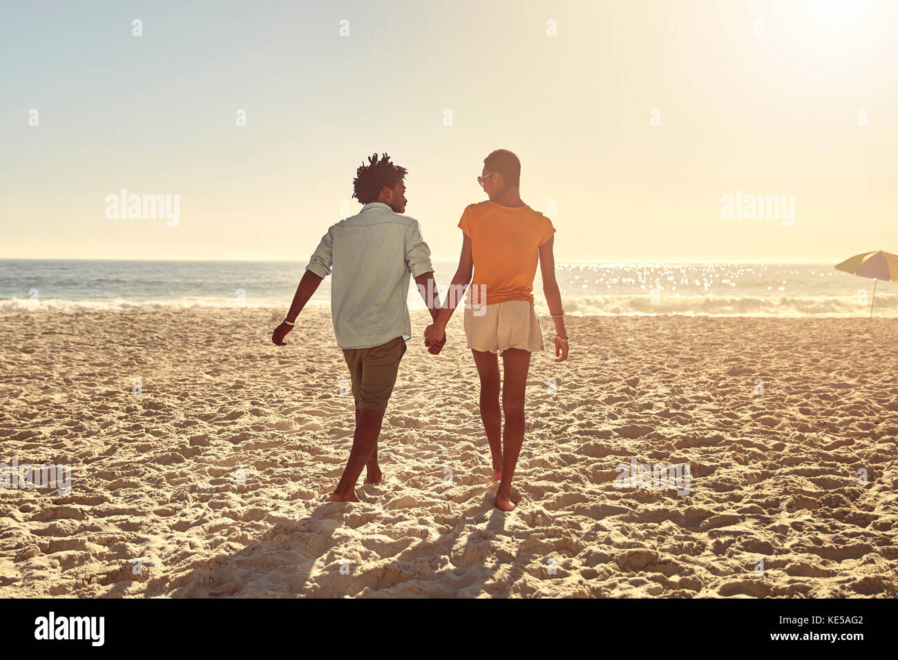 Junges Paar, das Hände hält und am sonnigen Sommerstrand spazierengeht Stockfoto