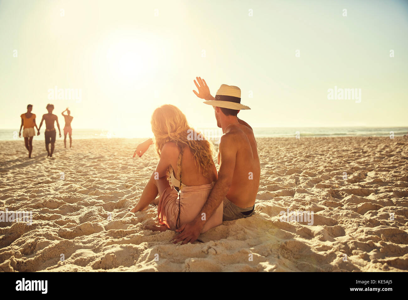 Junges Paar winkt Freunden am sonnigen Sommerstrand zu Stockfoto