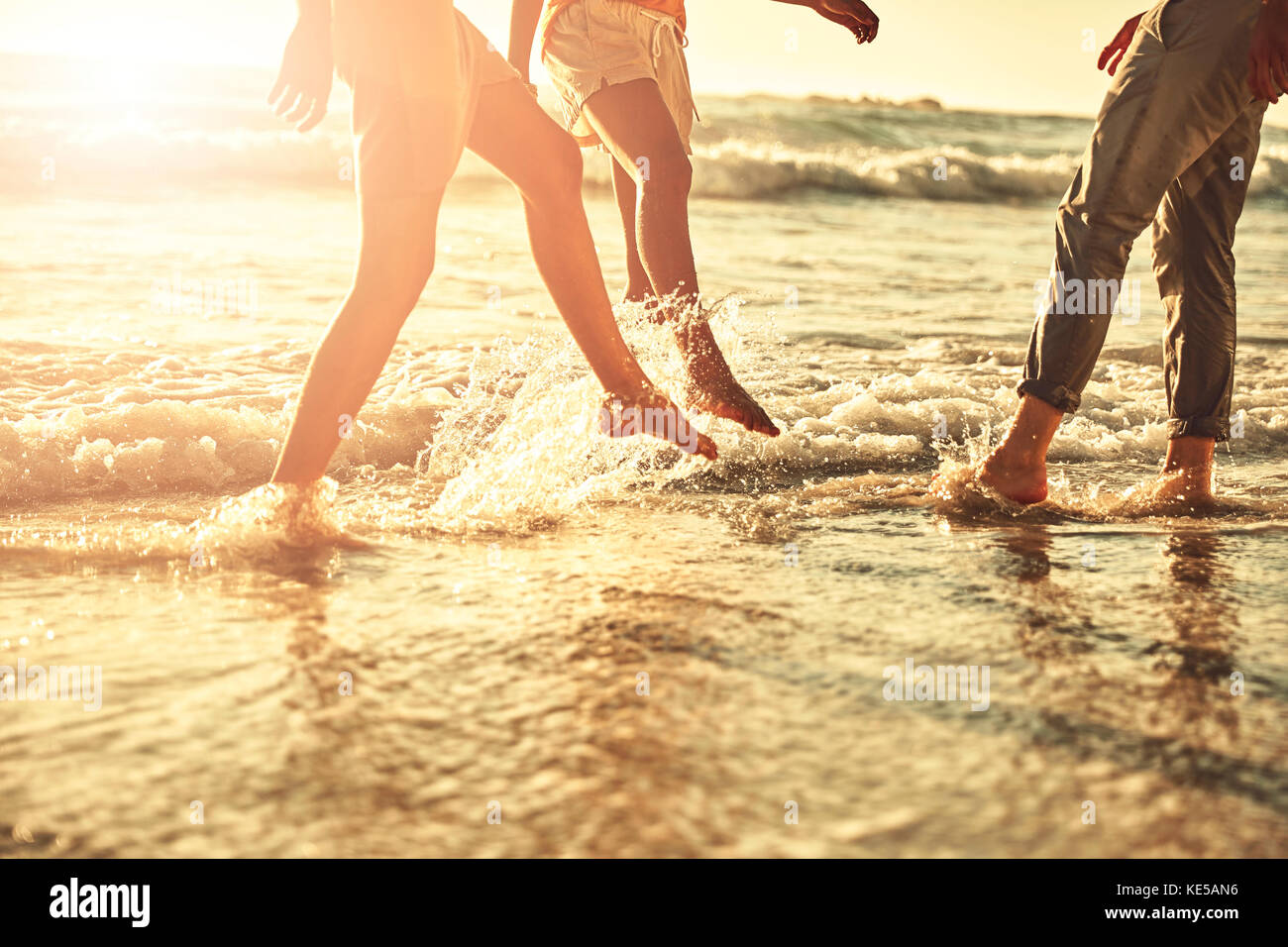 Junge Freunde planschen im sonnigen Sommer Meeresbrandung Stockfoto
