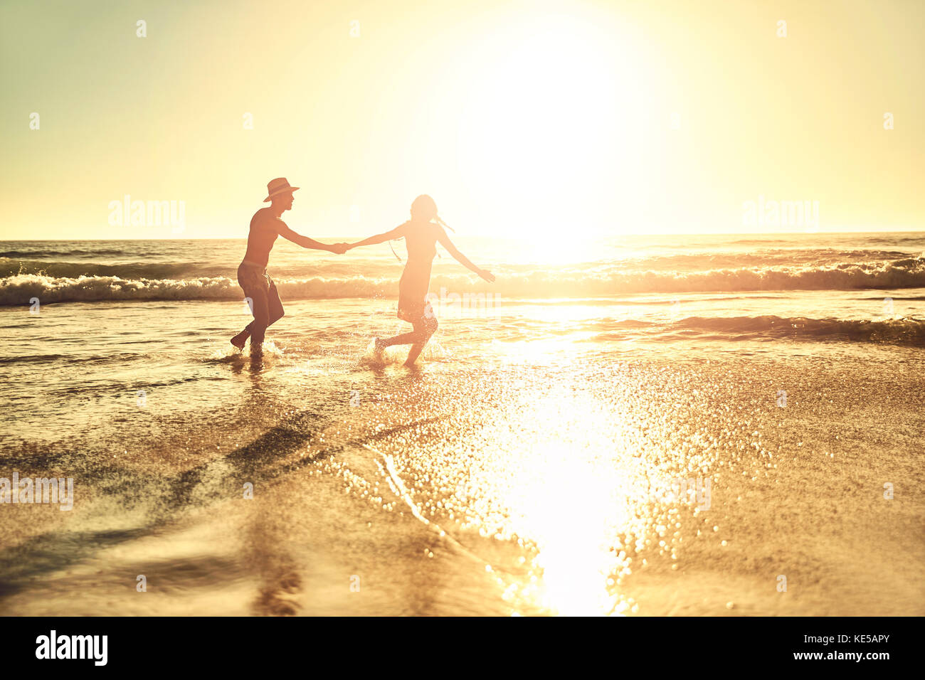 Junges Paar mit Händen, zu Fuß in sonnigen Sommer Sonnenuntergang Ozean Strand surfen Stockfoto