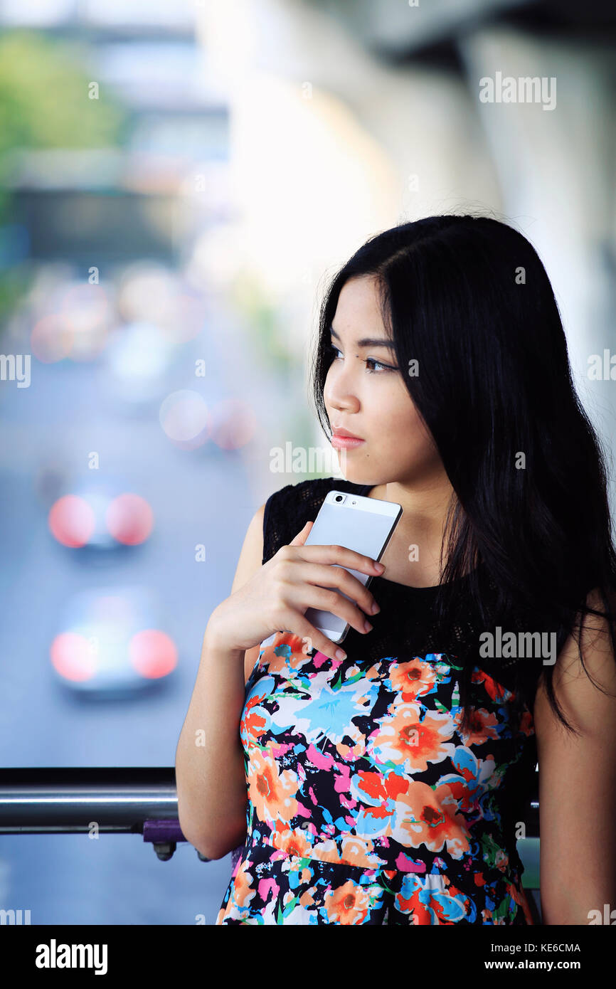 Asiatische Frau mit Telefon im Freien aus suchen Kamera Stockfoto