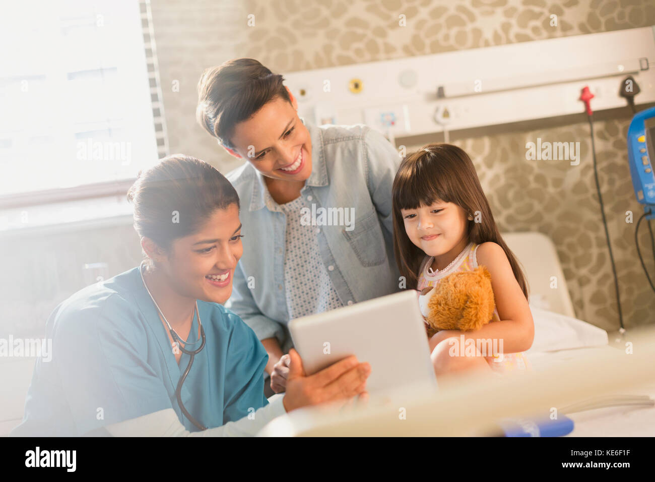 Krankenschwester zeigt digitale Tablette für Mädchen Patient und Mutter Im Krankenhauszimmer Stockfoto