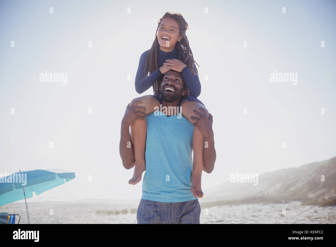 Verspielter Vater trägt Tochter auf Schultern am sonnigen Sommerstrand Stockfoto
