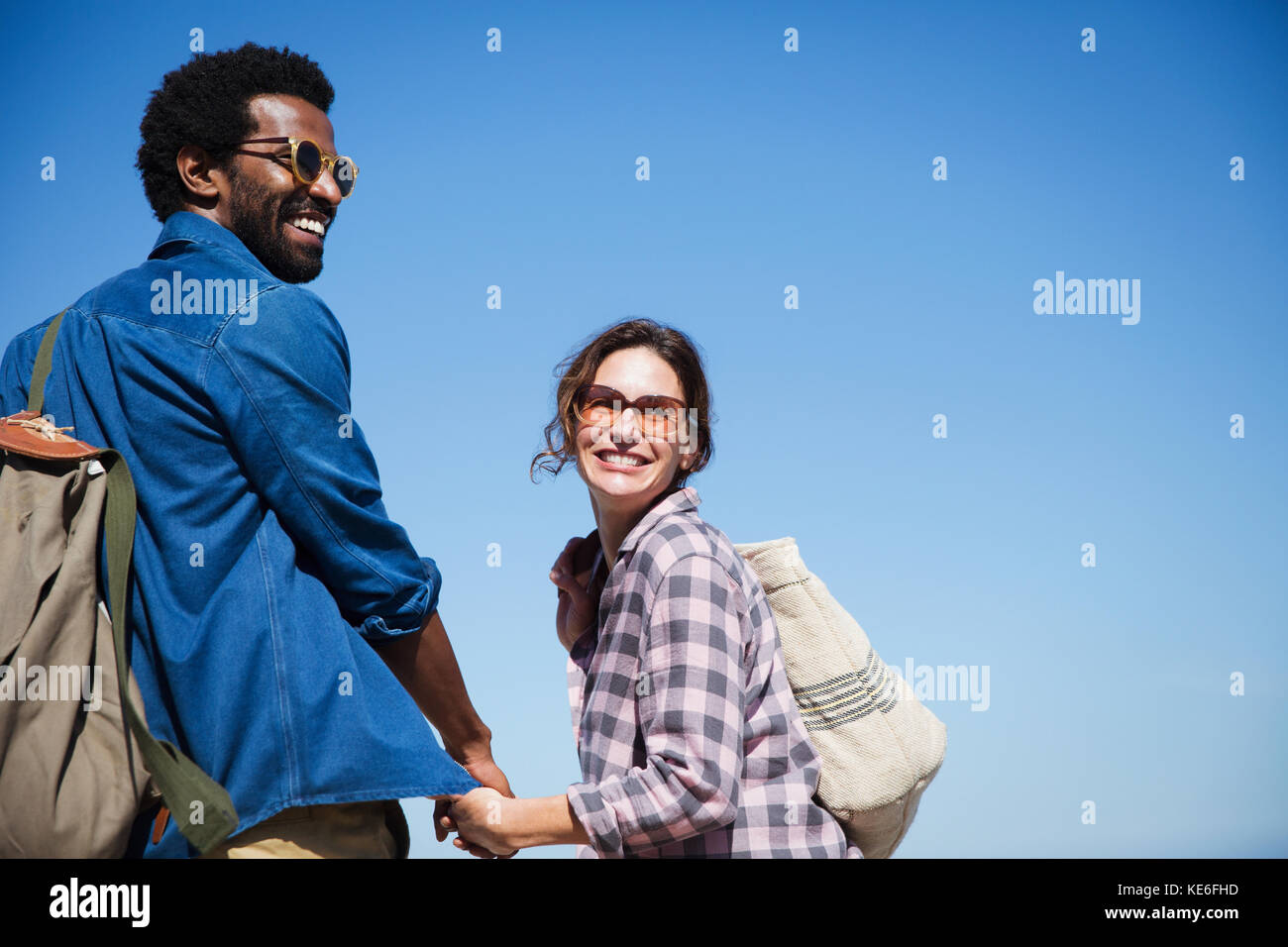 Portrait lächelndes, liebevolles multiethnisches Paar, das die Hände unter dem sonnigen, sommerblauen Himmel hält Stockfoto