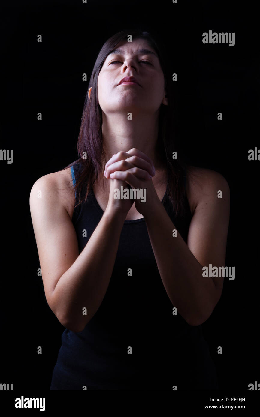 Treue Frau beten, Hände in der Anbetung gefaltet mit Kopf auf und geschlossenen Augen in religiösem Eifer für Gott, auf einem schwarzen Hintergrund. Gebet Gläubigen beten Stockfoto