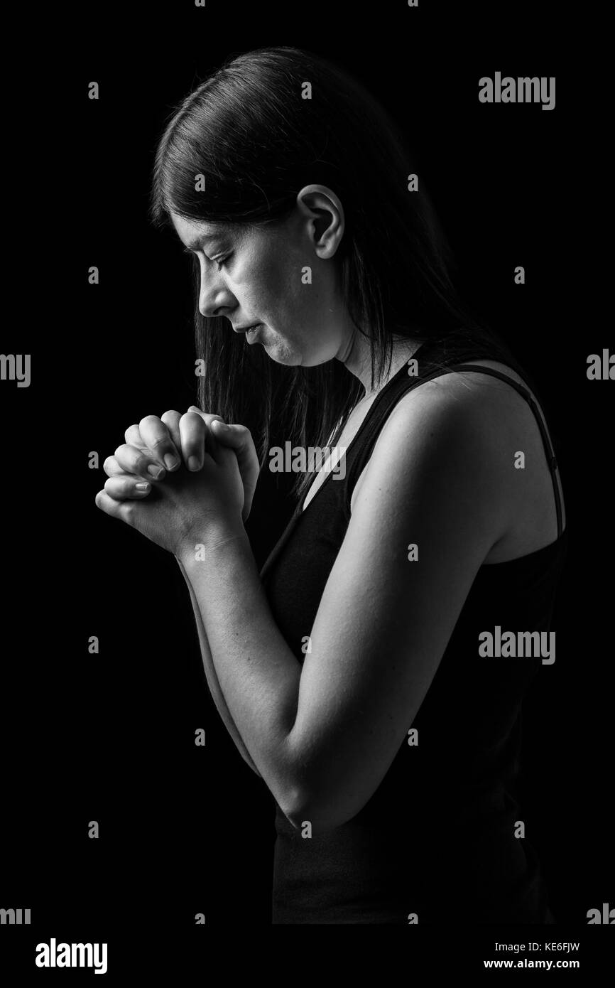 Treue Frau zu beten, die Hände gefaltet in der Anbetung mit Kopf nach unten zu Gott und Augen in religiöser Inbrunst geschlossen, auf einem schwarzen Hintergrund. Falten beten Gebet Stockfoto
