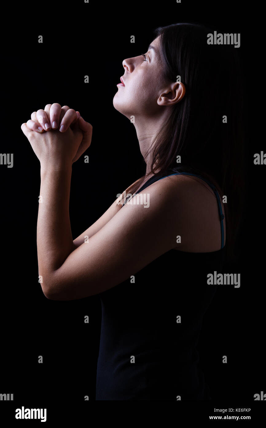 Treue Frau beten in Anbetung zu Gott suchen, in der Hoffnung, mit Hände gefaltet und religiöse Inbrunst auf einem schwarzen Hintergrund. beten Gebet hoffnungsvoll Falten Stockfoto