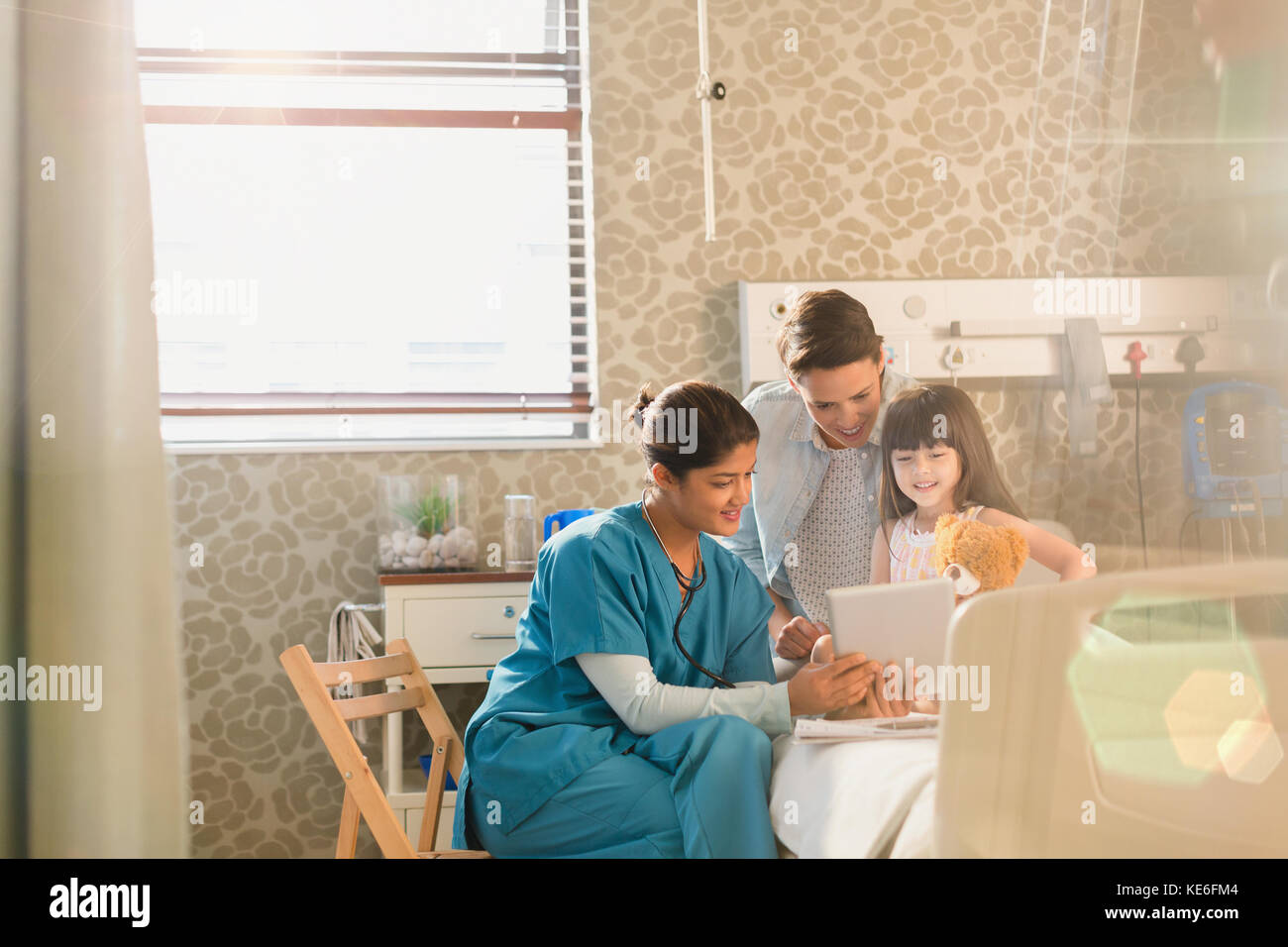 Krankenschwester zeigt digitale Tablette für Mädchen Patient und Mutter Im Krankenhauszimmer Stockfoto