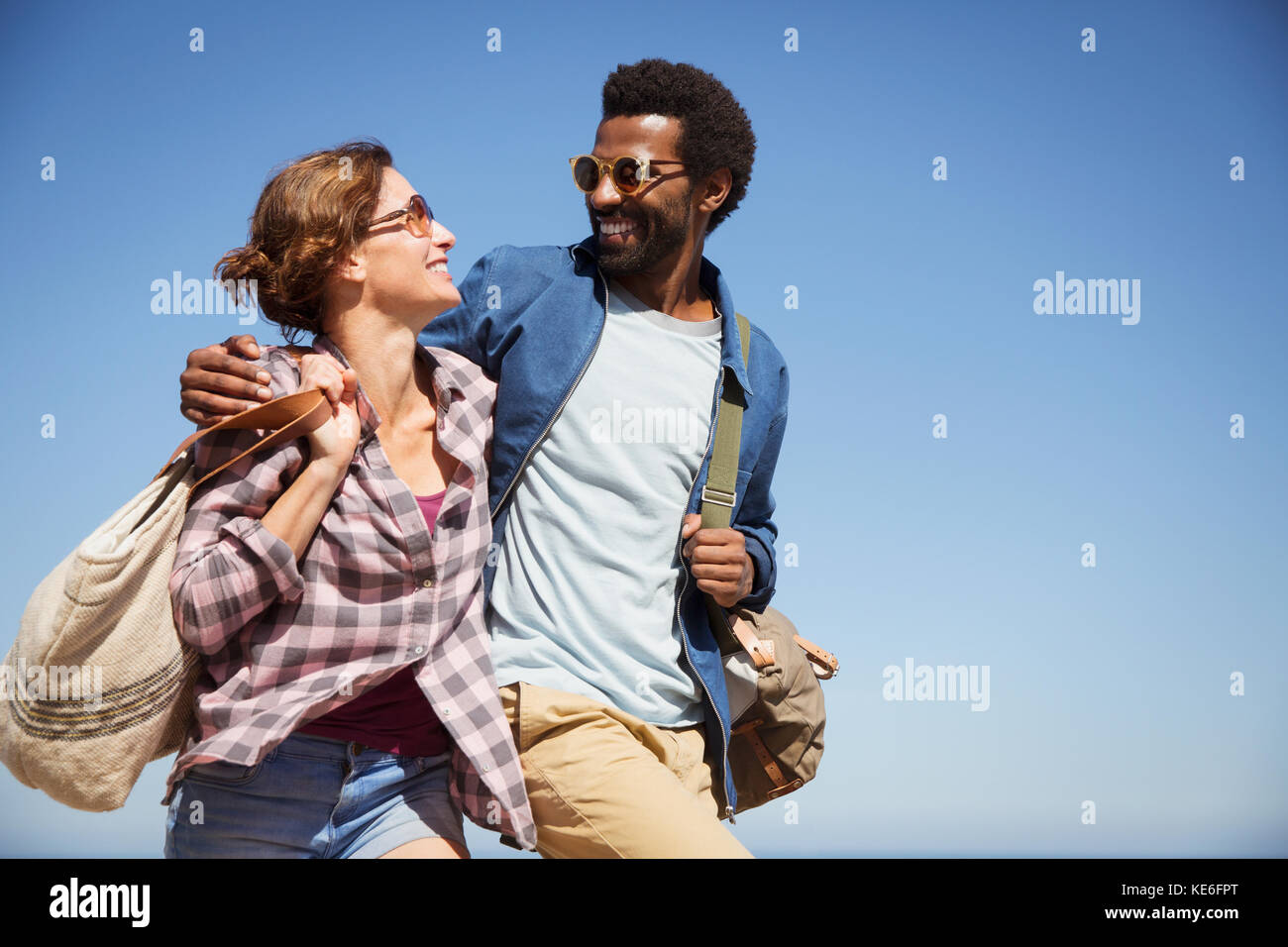 Liebevolles multiethnisches Paar umarmt und unter sonnigem Sommerblau spazierengeht Himmel Stockfoto