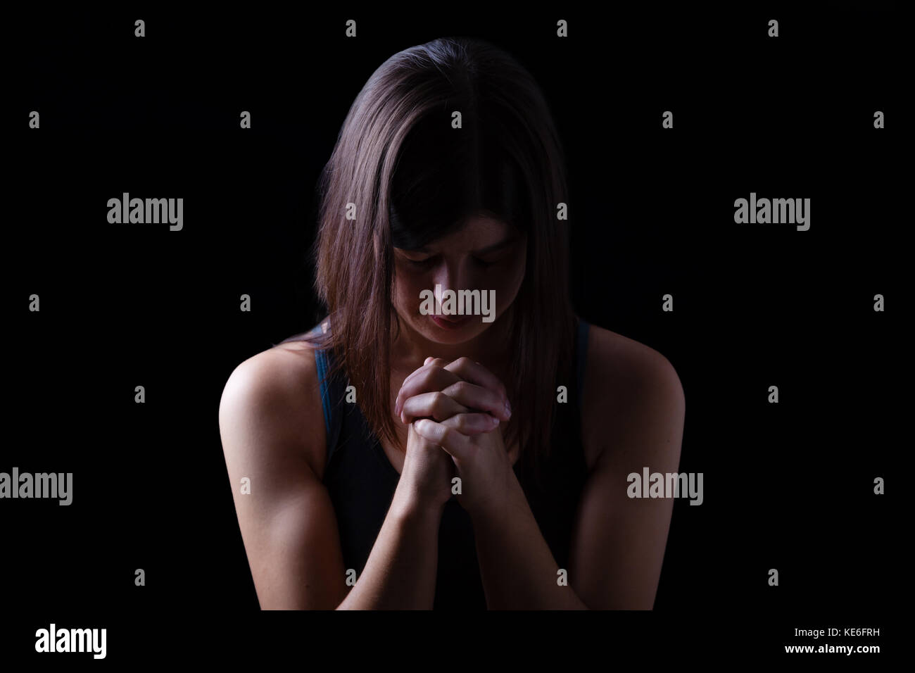 Gläubigen athletische Frau beten, mit Händen in Anbetung zu Gott gefaltet, Kopf und Augen in religiöser Inbrunst geschlossen, auf Low Key schwarzen Hintergrund. Beten Stockfoto