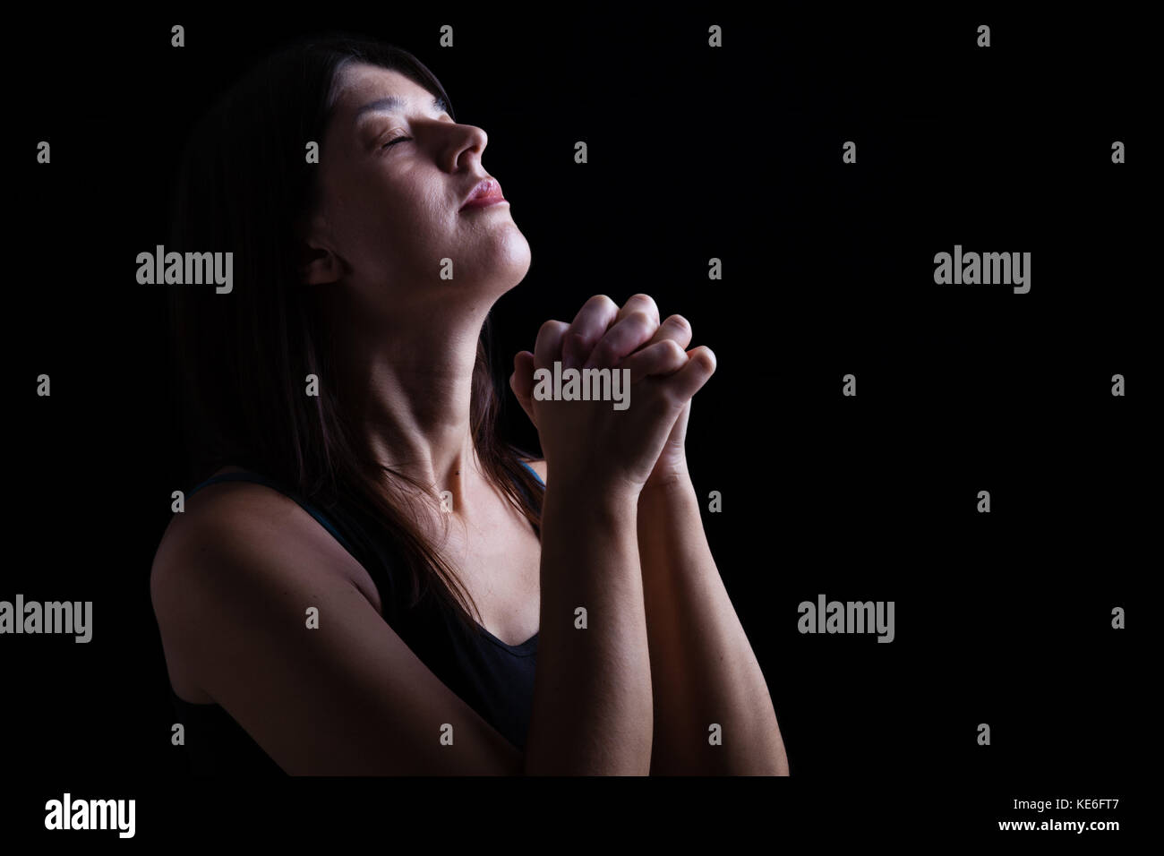 Eine treue Frau schließen, zu beten, die Hände gefaltet in der Anbetung, Kopf, geschlossenen Augen in religiöser Inbrunst. schwarzer Hintergrund Gebet christlichen religiösen Stockfoto