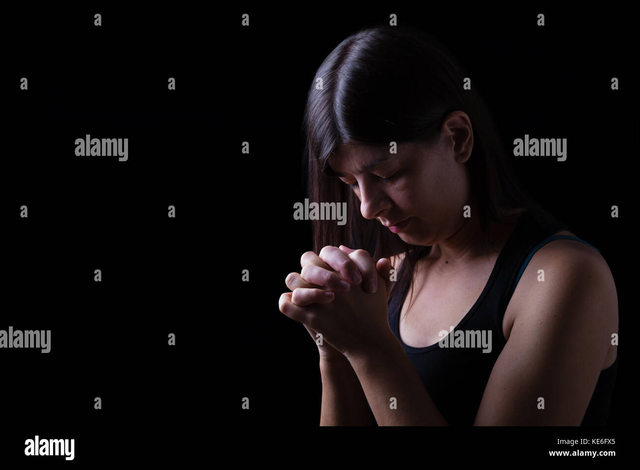 Treue Frau beten, Hände in der Anbetung zu Gott gefaltet, Kopf nach unten, die Augen geschlossen, in religiöser Inbrunst. schwarzer Hintergrund Gebet geschlossenen Augen die christliche Hoffnung Stockfoto