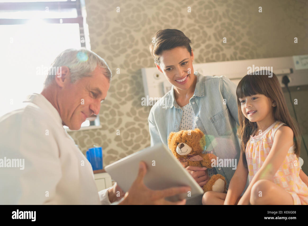 Männlich Arzt zeigt digitale Tablette Mädchen Patienten und Mutter Im Krankenhauszimmer Stockfoto