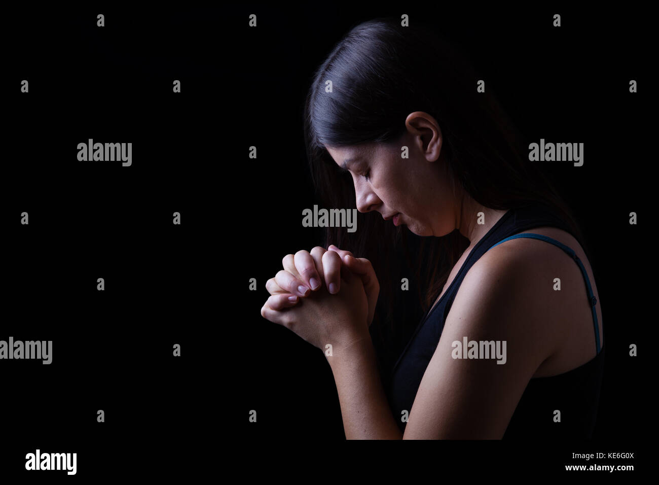 Treue Frau beten, Hände in der Anbetung zu Gott gefaltet, Kopf nach unten, die Augen geschlossen, in religiöser Inbrunst. schwarzer Hintergrund Gebet geschlossenen Augen die christliche Hoffnung Stockfoto